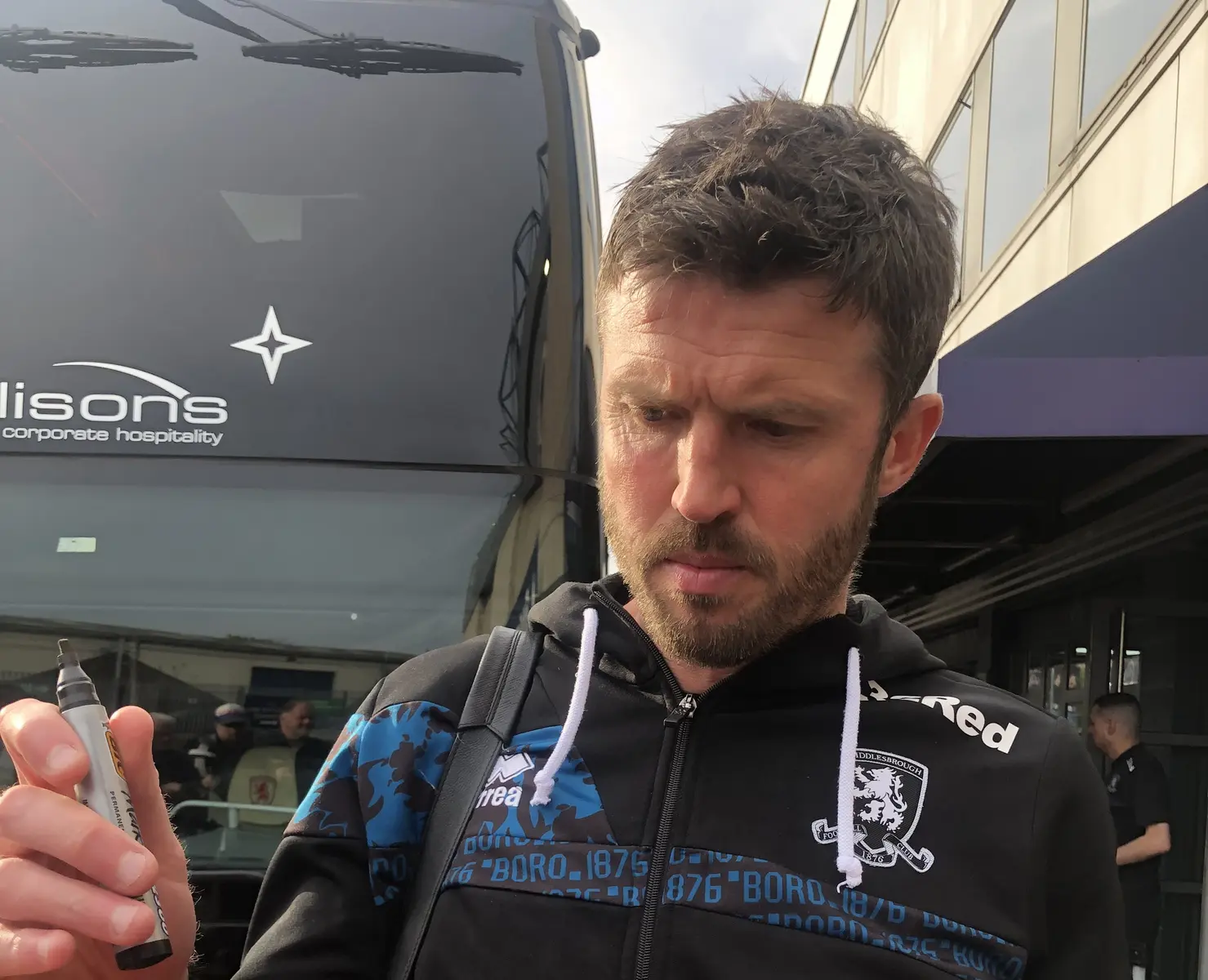 Michael Carrick veste um casaco preto do Middlesbrough FC ao lado de um autocarro.